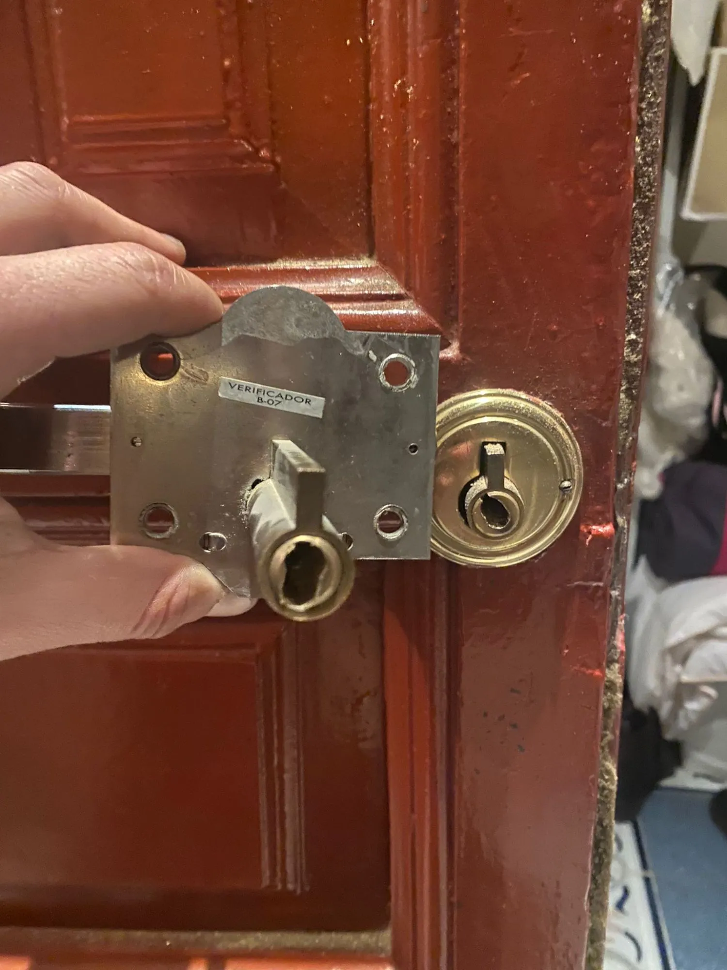 Cerradura retirada de una puerta de madera roja en Boadilla del Monte, con el bombín dañado y el escudo todavía en la puerta.