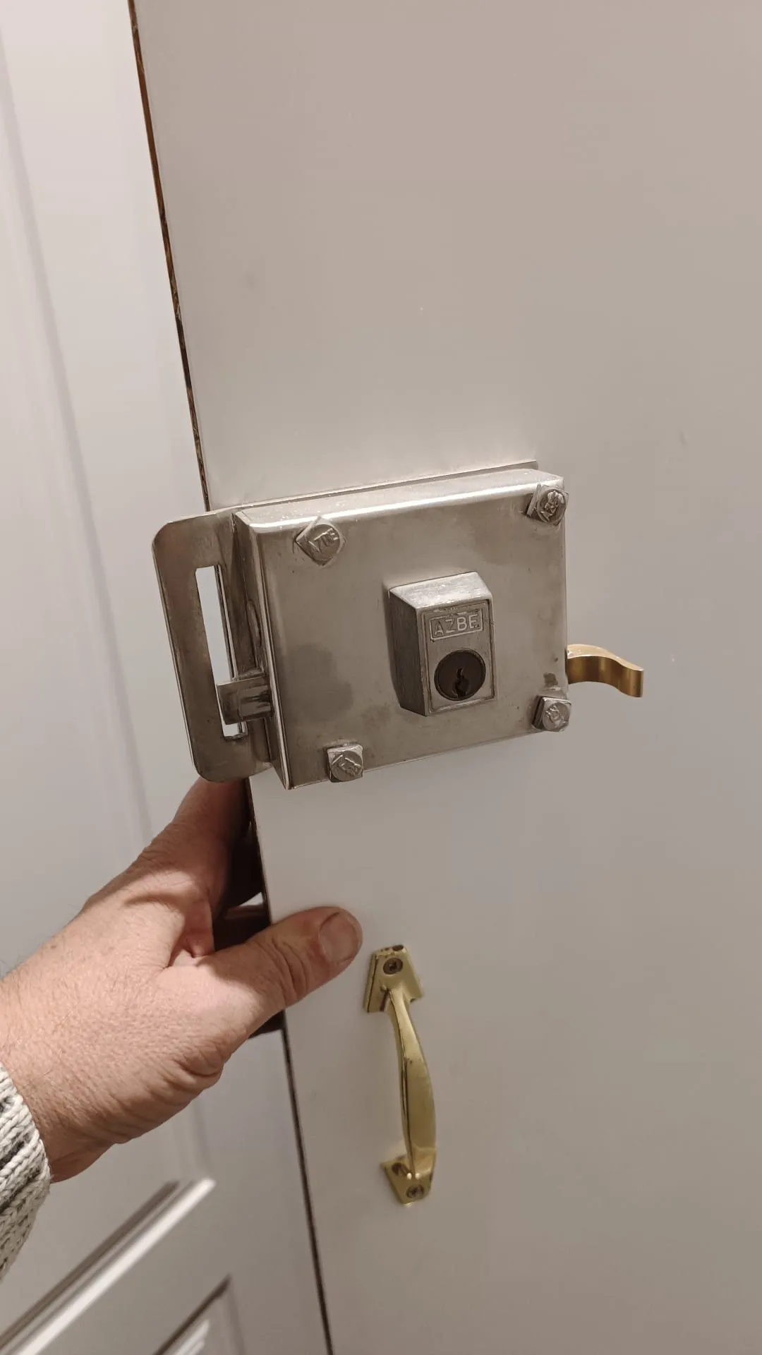 Cerradura de sobreponer AZBE en una puerta blanca en Barajas, con su cerradero y un tirador dorado debajo.