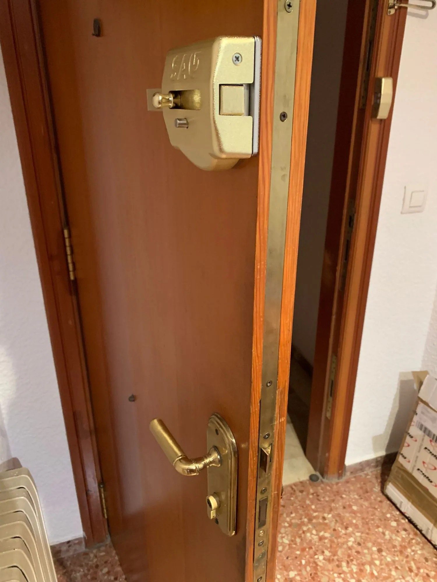Puerta de madera abierta en Majadahonda, con un cerrojo de sobreponer SAG dorado en la parte alta, la cerradura en el canto y la manilla con su placa.